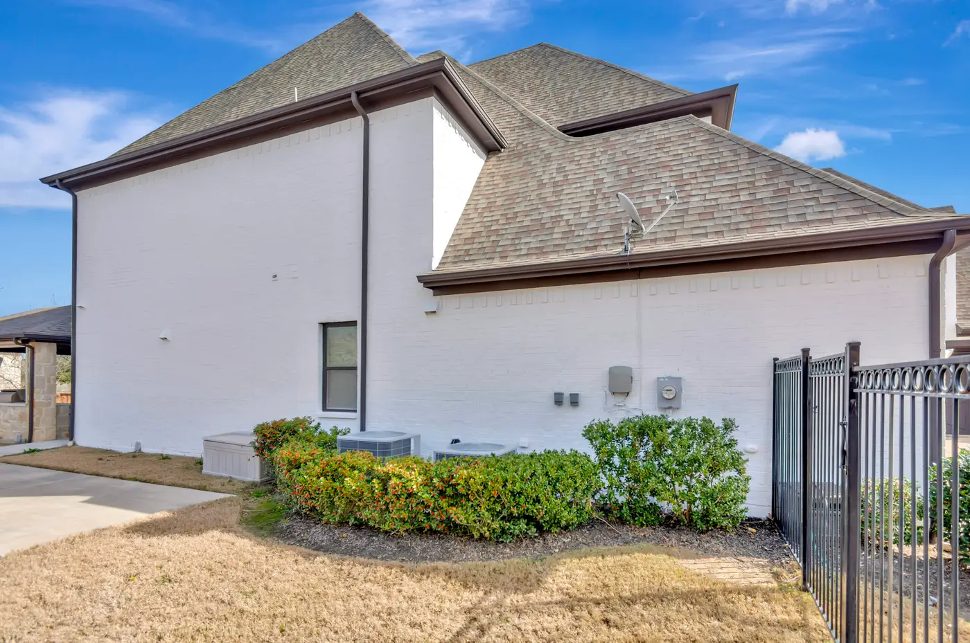 Side elevation of a white painted brick home with air-conditioning units and an iron fence