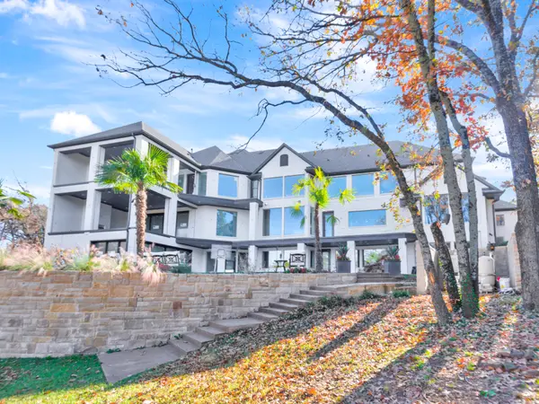 Three-story white painted home above a stone retaining wall and steps, with autumn trees
