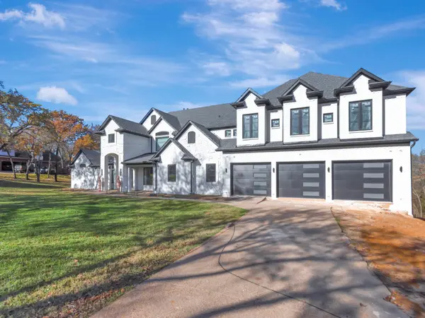 Painted brick and stone home from the drive, with a run of dark glazed garage doors
