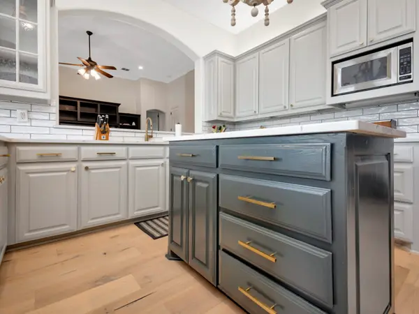 Gray painted island drawers with brass pulls, against pale painted wall cabinets