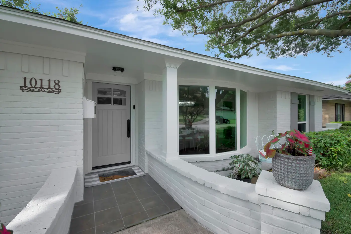 White painted entry with a slab front door, square column and a low painted brick planter