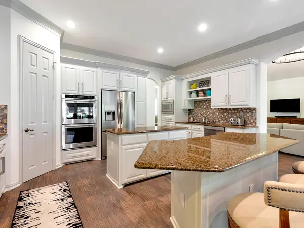 Kitchen with white painted cabinetry, double ovens and a granite-topped island