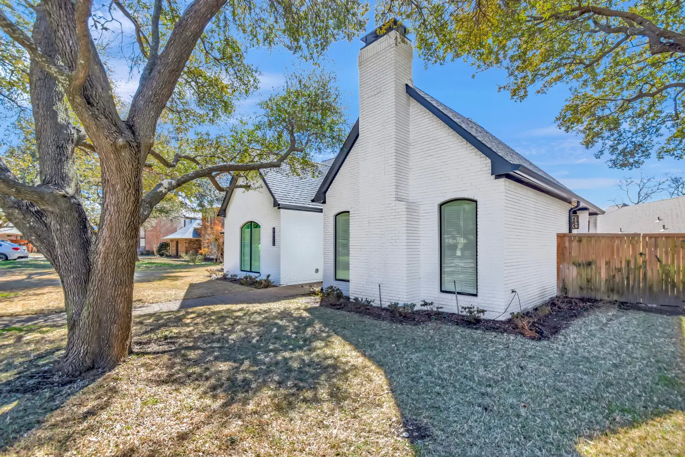 White painted brick gable with a chimney and tall arched windows, beside a mature oak