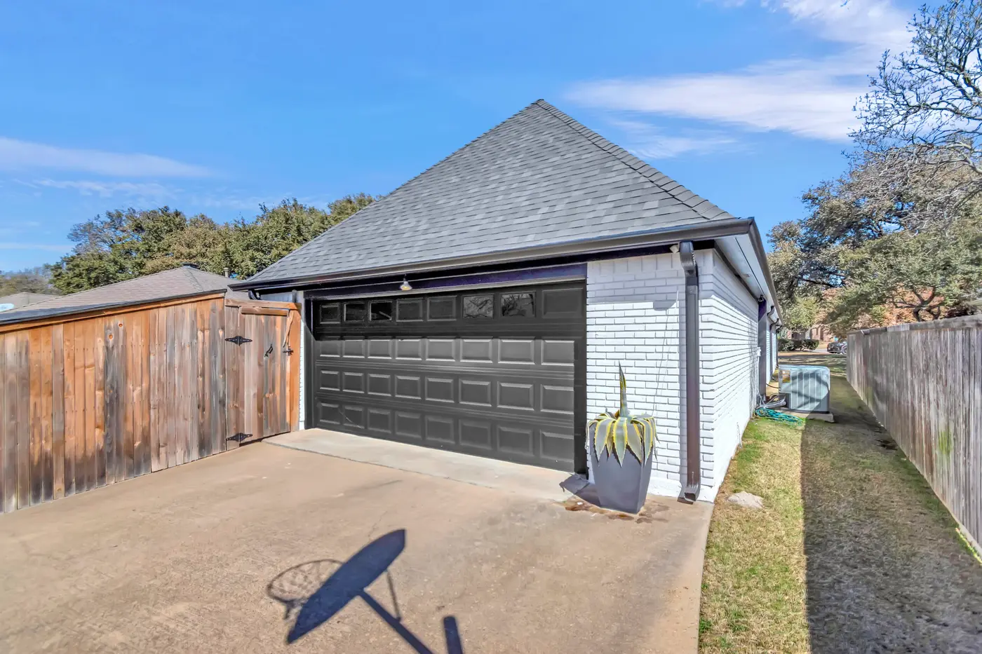 Detached garage in white painted brick with a dark paneled door, between timber fences