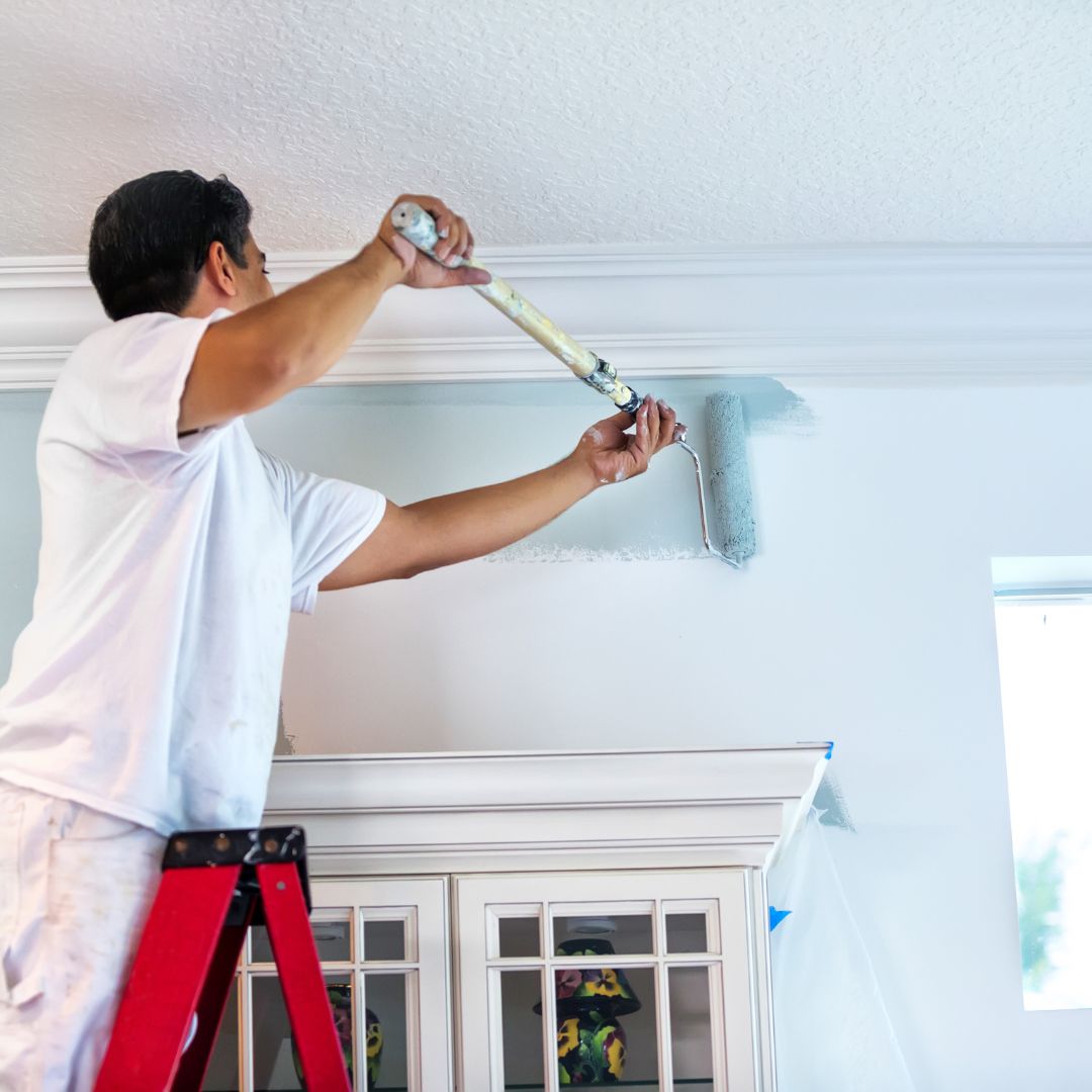 Man on a ladder painting a wall around wood trim